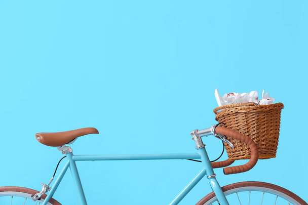 Modern bicycle with wicker basket, book and flowers on blue background - Photo, image