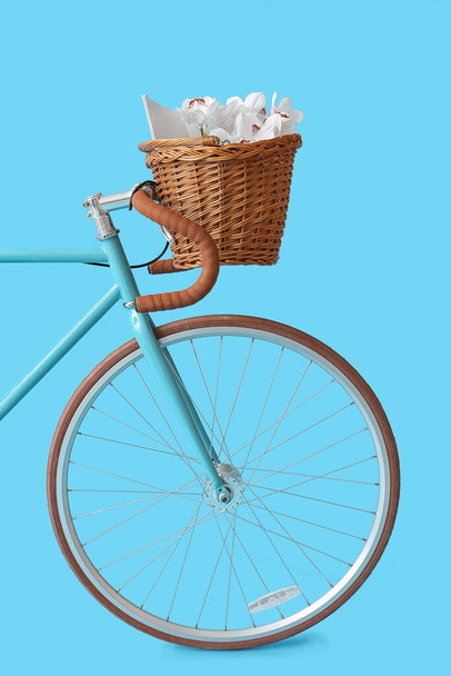 Bicicleta moderna con cesta de mimbre, libro y flores sobre fondo azul - Foto, Imagen