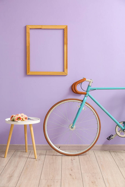 Tavolo con fiori e bicicletta vicino alla parete lilla - Foto, immagini