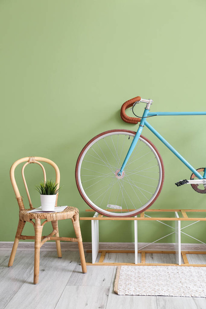 Стул с ковровым покрытием, стенд и велосипед возле зеленой стены - Фото, изображение