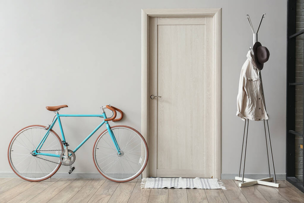 Moderne fiets en rek met kleding in de buurt van lichte muur in hal - Foto, afbeelding