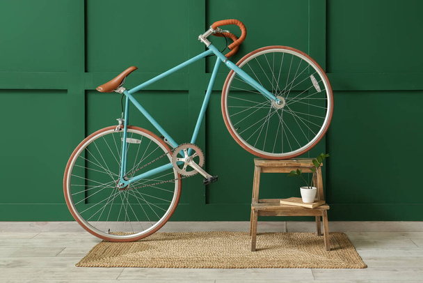Bicicletta moderna, scala con libro e vaso da fiori vicino alla parete verde - Foto, immagini