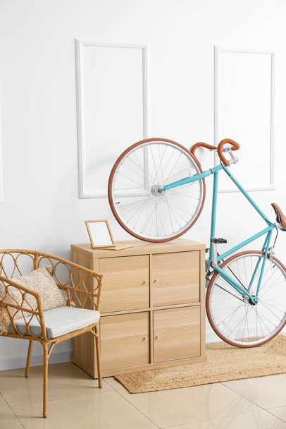 Moderne fiets met ladekast en stoel bij witte muur - Foto, afbeelding