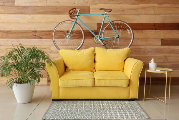Interior of stylish living room with yellow sofa, bicycle and wooden wall - 写真・画像