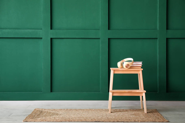 Sgabello in legno con cuffie e libri vicino alla parete verde - Foto, immagini