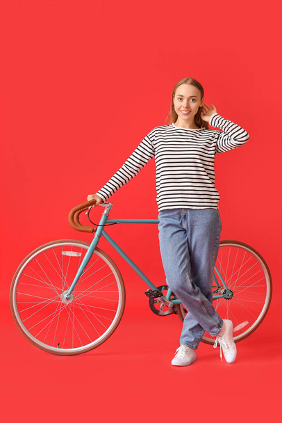 Pretty teenage girl with bicycle on red background - Fotografie, Obrázek