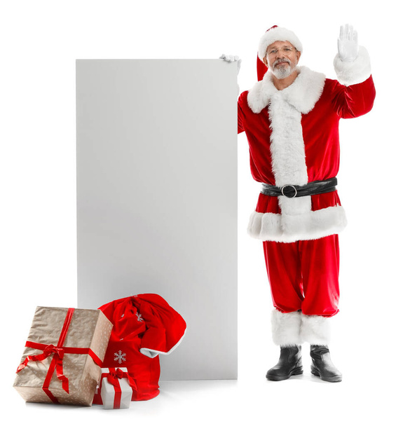 Санта-Клаус с большой пустой картой и подарочные коробки размахивая рукой на белом фоне - Фото, изображение