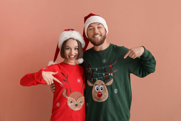 Щаслива молода пара в стильний різдвяний одяг і капелюхи Санта Клауса на кольоровому тлі - Фото, зображення
