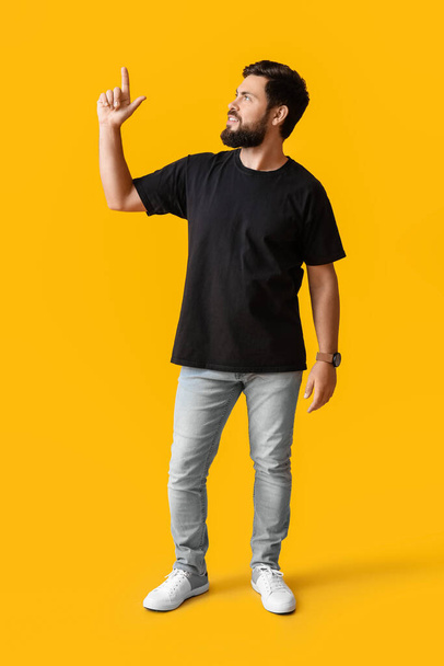 Handsome man in black t-shirt pointing at something on yellow background - Foto, Imagen