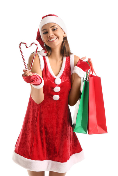 Beautiful woman in Santa costume, with candy canes and shopping bags on white background - Photo, Image