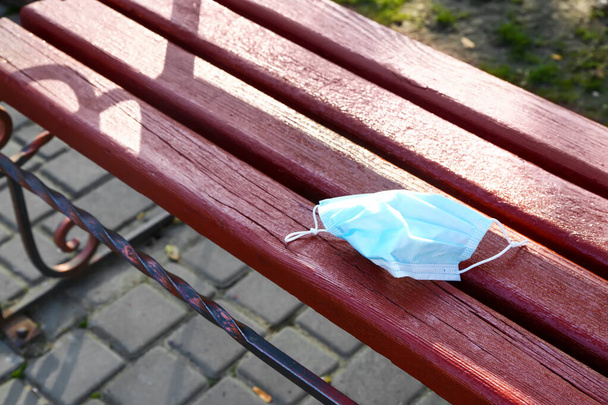 Gebruikt medisch masker op bank in park - Foto, afbeelding