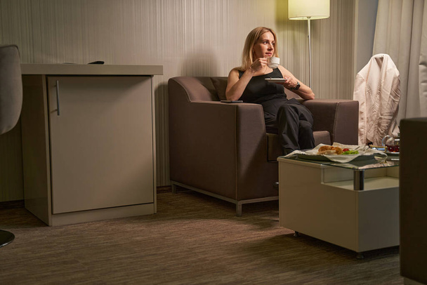 Feminino descansando na poltrona do quarto de hotel com xícara de café - Foto, Imagem