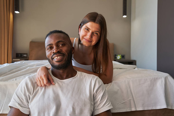 Happy mixed-race couple posing for camera in bedroom - Fotografie, Obrázek