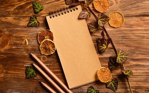 Quaderno con matite, fette di limone essiccate e ramo vegetale su fondo di legno scuro - Foto, immagini
