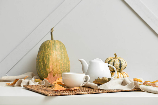 Tetera, taza de bebida caliente y hojas de otoño en la mesa cerca de la pared gris - Foto, imagen