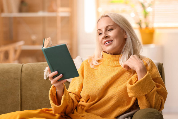 Beautiful mature woman reading book at home on autumn day - Fotó, kép