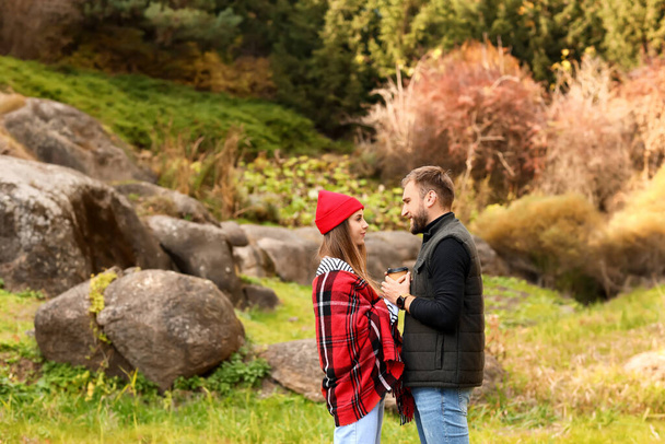 Sonbahar parkında birbirlerine bakan ellerinde kağıt bardakla sevgili bir çift. - Fotoğraf, Görsel