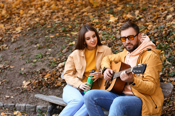 Egy fiatalember gitározik a barátnőjének az őszi parkban. - Fotó, kép