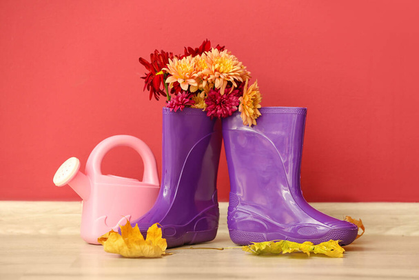 Gumové boty, zavlažovací plechovky a květiny na podlaze proti barevné stěně - Fotografie, Obrázek