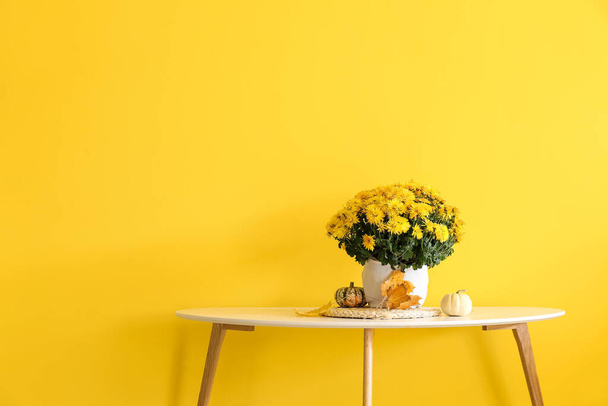 Pot with beautiful Chrysanthemum flowers on table near yellow wall - Fotografie, Obrázek