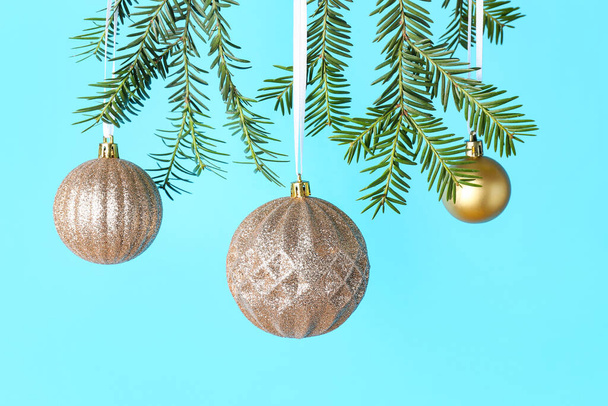 Beautiful Christmas balls hanging on fir branches against color background, closeup - Photo, Image