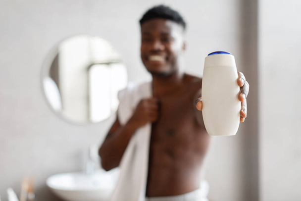 Unerkennbarer schwarzer Kerl zeigt Duschgelflasche im Badezimmer - Foto, Bild