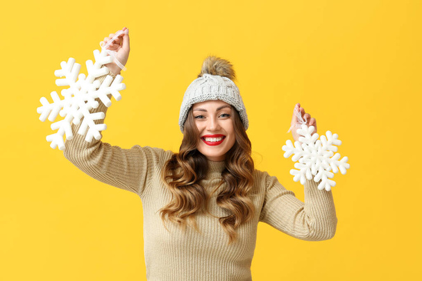 Happy young woman holding snowflakes on yellow background - Photo, Image