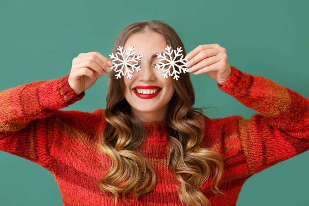 Beautiful smiling woman in warm sweater holding snowflakes near face on green background - Photo, Image
