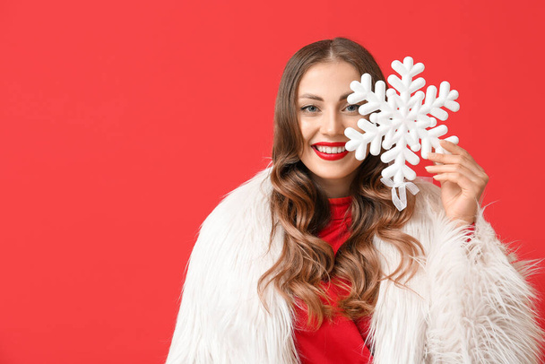 Donna sorridente alla moda che tiene il fiocco di neve grande vicino a faccia su sfondo rosso - Foto, immagini