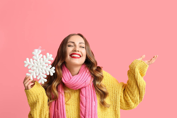 Happy woman holding snowflake and pointing at something on color background - Photo, Image