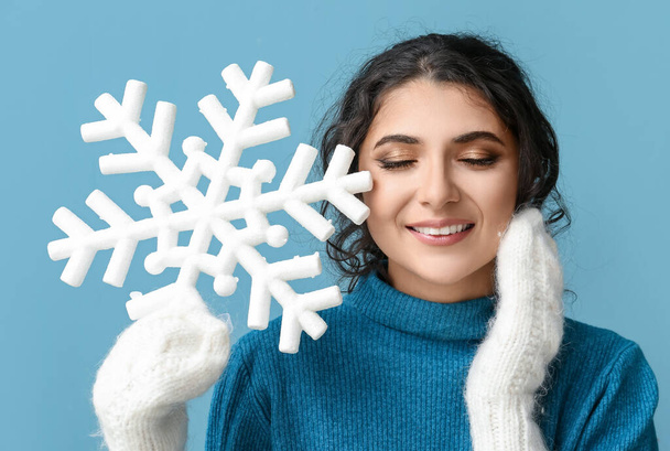 Beautiful woman with closed eyes holding big snowflake and touching her face with hand on blue background - Photo, Image