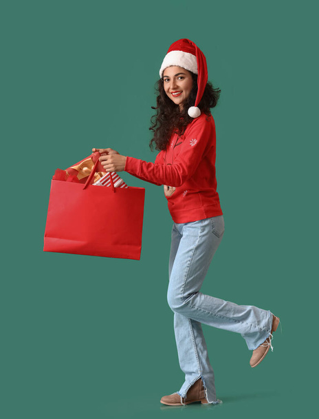 Krásná chůze mladá žena v klobouku Santa a s nákupní taškou na barevném pozadí - Fotografie, Obrázek