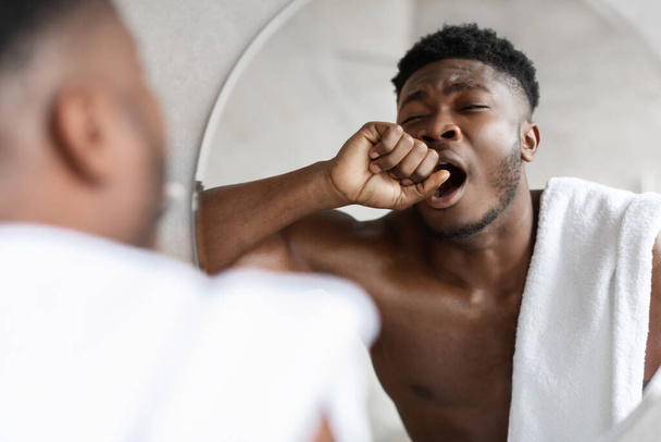 Somnolent Afro-Américain bâillant debout près du miroir dans la salle de bain - Photo, image