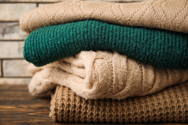 Stack of different knitted sweaters on wooden table against brick wall background, closeup - Fotó, kép