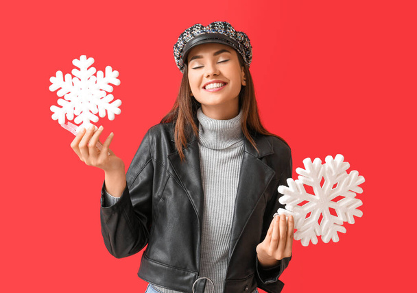 Beautiful woman in cap with big snowflakes on red background - Photo, Image