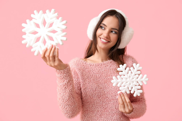 Beautiful woman in earmuffs with snowflakes on pink background - Photo, Image