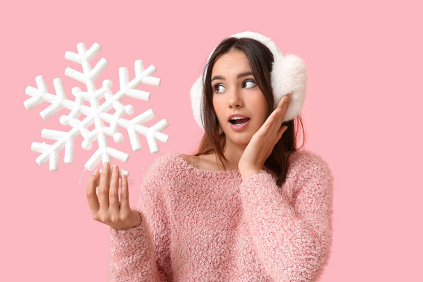 Surprised young woman in earmuffs with snowflake on pink background - Fotó, kép