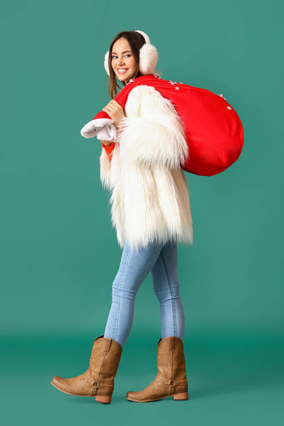 Mooie wandelende jonge vrouw met Santa tas op kleur achtergrond - Foto, afbeelding