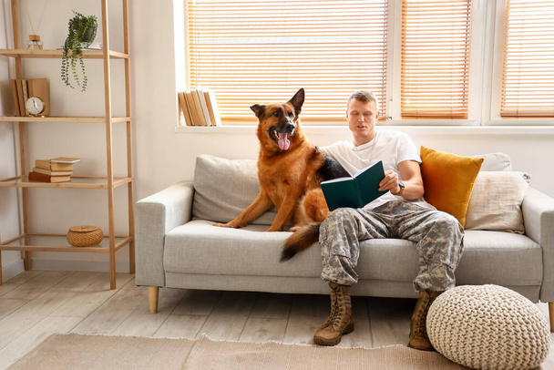 Солдат армии США с военной рабочей собакой читает книгу дома - Фото, изображение