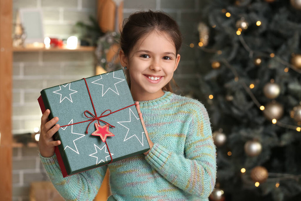 Schattig klein meisje met cadeau thuis op kerstavond - Foto, afbeelding