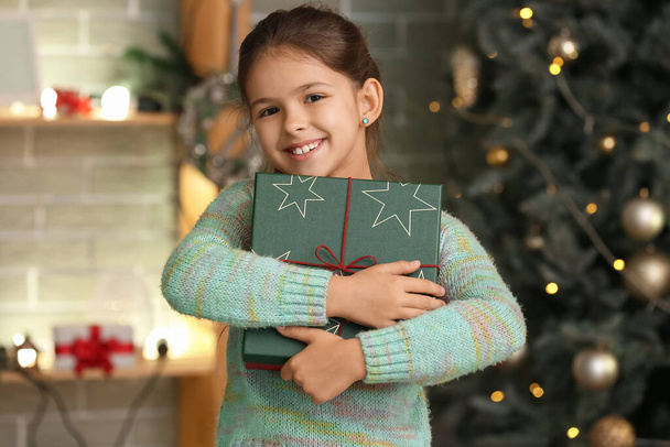 Schattig klein meisje met cadeau thuis op kerstavond - Foto, afbeelding