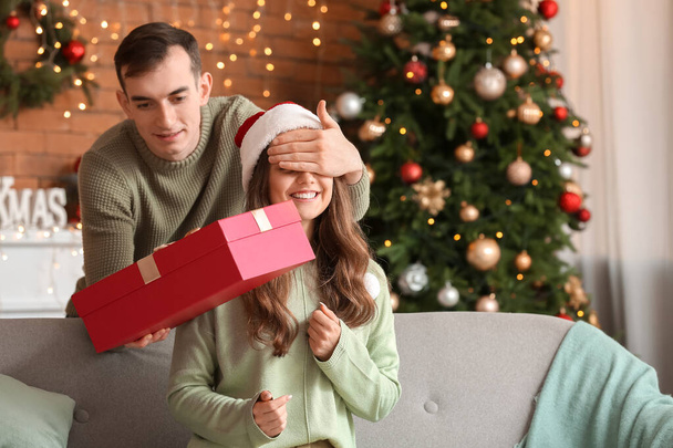 Ο νεαρός χαιρετάει την κοπέλα του παραμονή Χριστουγέννων στο σπίτι. - Φωτογραφία, εικόνα