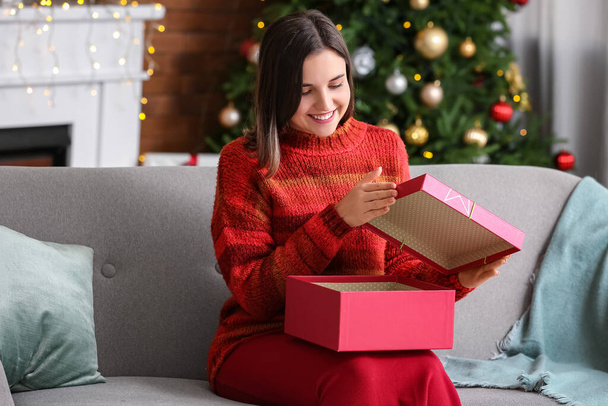 Kaunis nuori nainen avaamalla lahja kotona jouluaattona - Valokuva, kuva