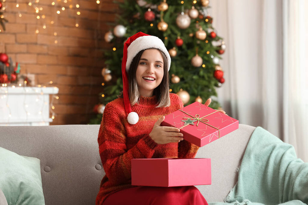 Mooie jonge vrouw opening cadeau thuis op kerstavond - Foto, afbeelding