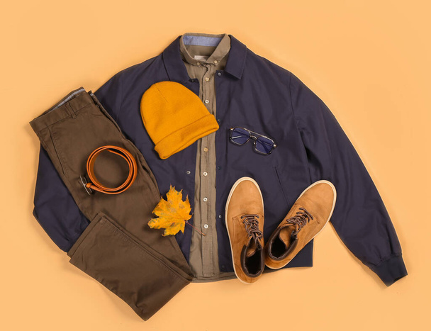 Chaqueta masculina con estilo, pantalones, cinturón, sombrero, zapatos y hoja de otoño en el fondo de color - Foto, imagen