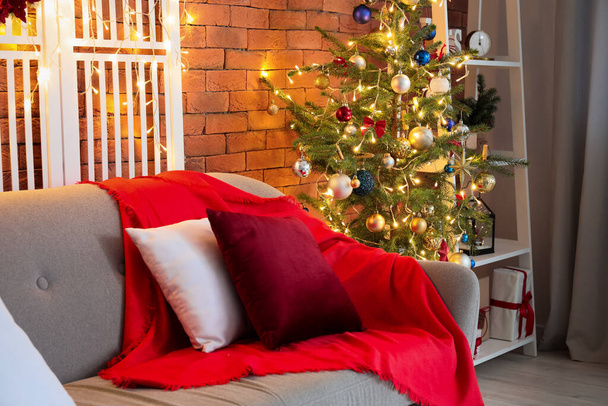 Parlayan ışıkları ve tuğla duvarın yanındaki kanepesi olan güzel Noel ağacı. - Fotoğraf, Görsel