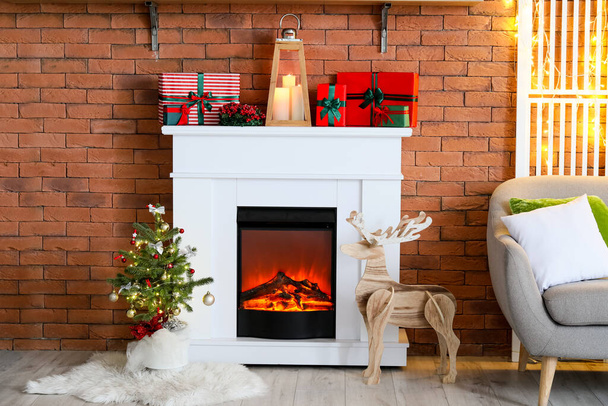Fireplace with gifts, wooden reindeer and small Christmas tree near brick wall - Photo, Image