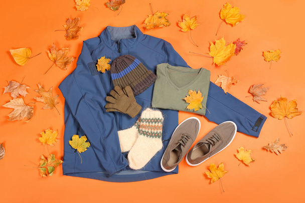 Chaqueta masculina, sombrero, guantes, suéter, calcetines, zapatos y hojas de otoño sobre fondo de color - Foto, imagen