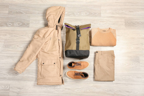 Stijlvolle herenjas, rugzak, schoenen, trui en broek op lichte houten achtergrond - Foto, afbeelding