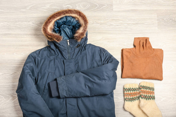 Kurtka zimowa, sweter i skarpetki na jasnym drewnianym tle - Zdjęcie, obraz